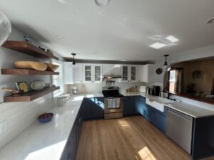 Modern kitchen with open shelves, blue and white cabinets, stainless appliances, and sunlit wooden floor.