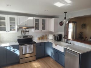 Modern kitchen with white and blue cabinets, stainless steel appliances, and sunlight on countertop.