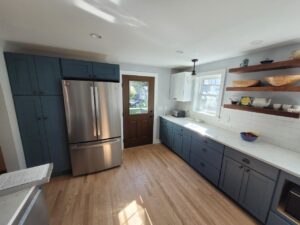 Modern kitchen with blue cabinets, stainless steel fridge, open shelves, and a wooden door leading outside.